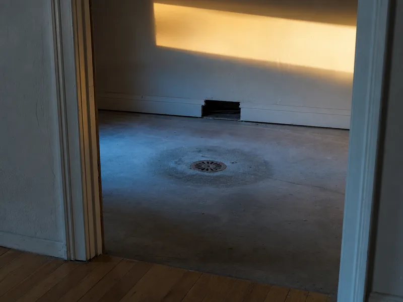 A cast-iron floor drain set into a basement slab with a dark dried tide line staining the concrete in a ring around it